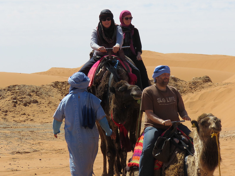a group of people riding camels through the desert merzouga